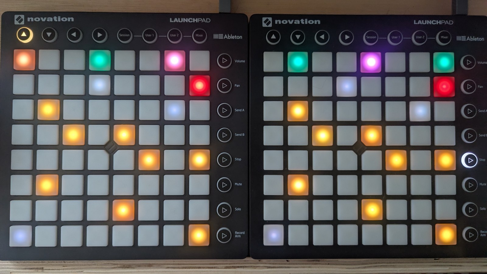 A locked jam keyboard: the same eight mustard held-note pads form a rising shape on both Launchpads, three slate octave markers remain visible on each LP, the row-7 freeze pads are red, and the top row carries a six-cell coloured gate pattern, photographed on the hardware